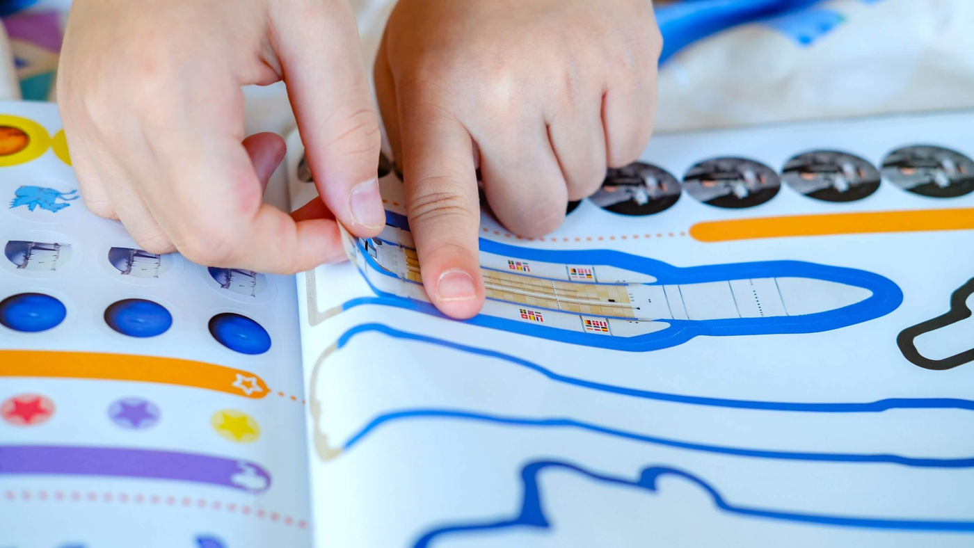 close up of kid playing a game inside an activity & sticker book