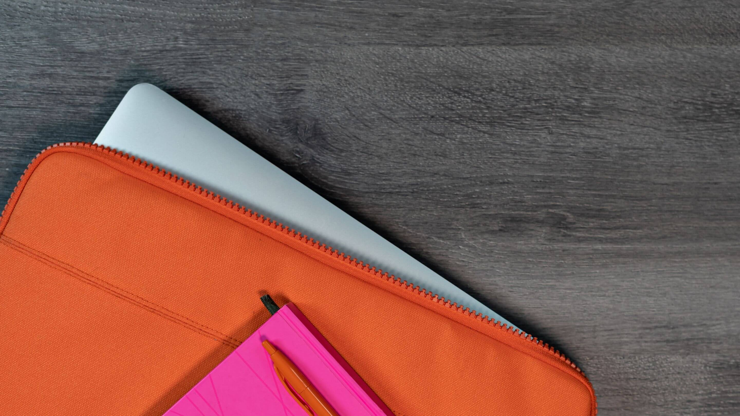silver laptop inside a bright orange laptop sleeve on a grey desk