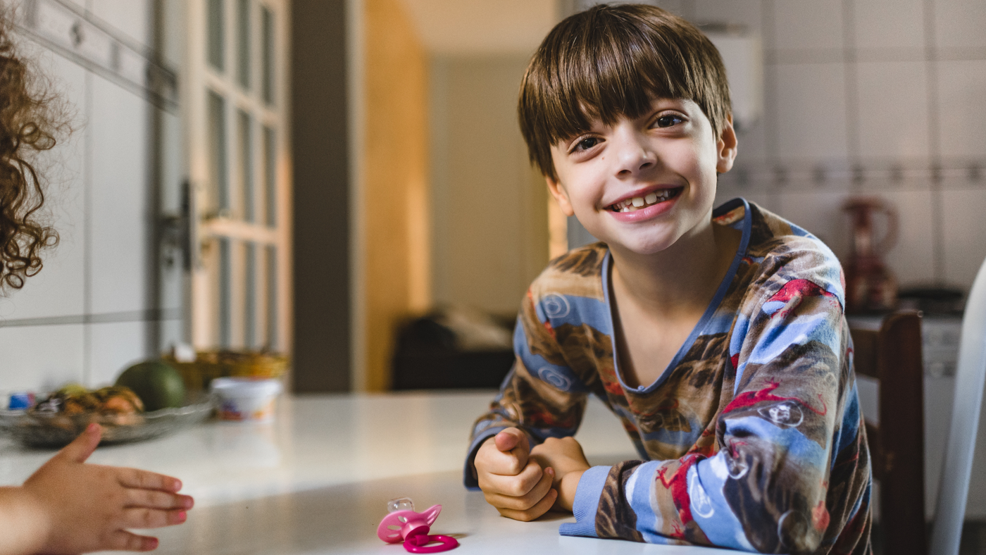 little boy wearing pyjama set sitting at dining table in kitchen