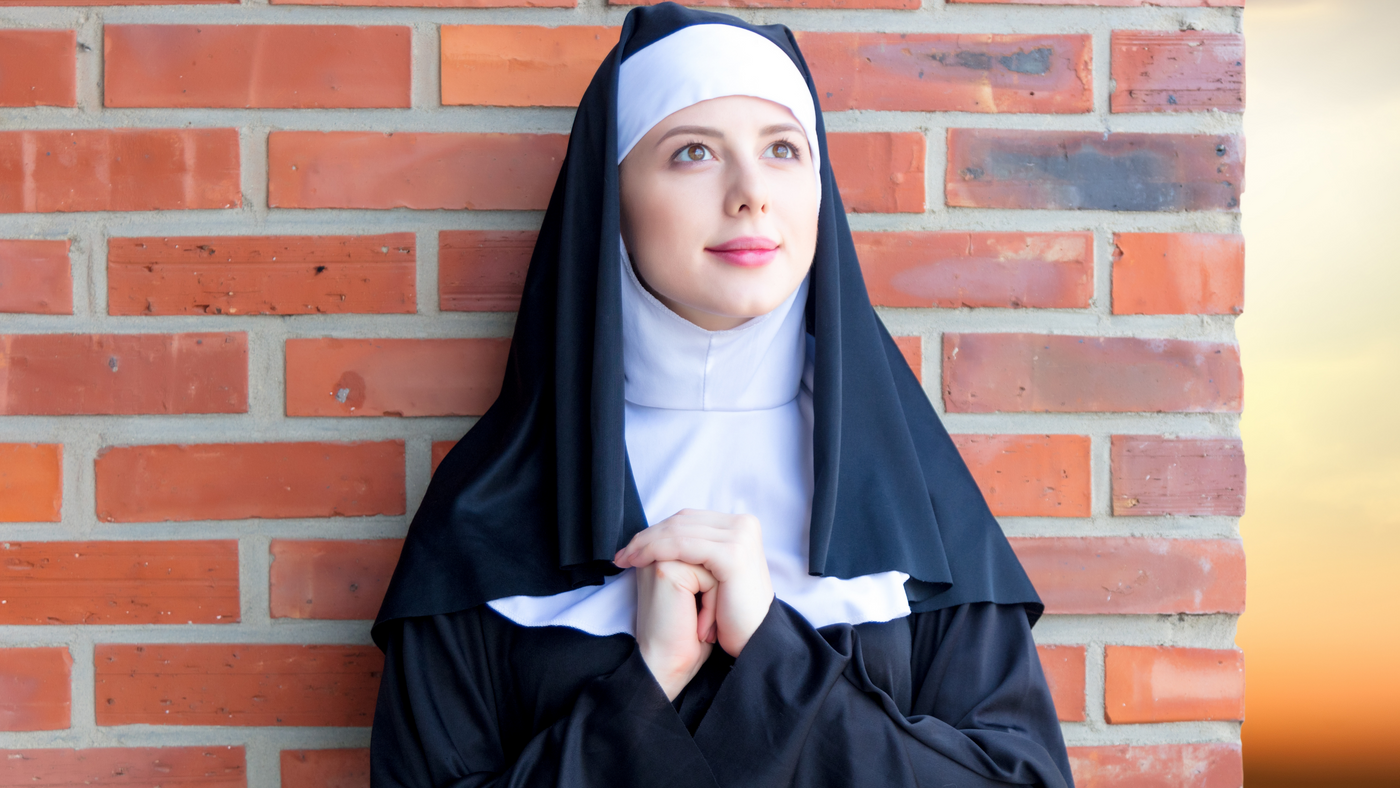 lady dressed as a nun standing in front of a brick wall praying