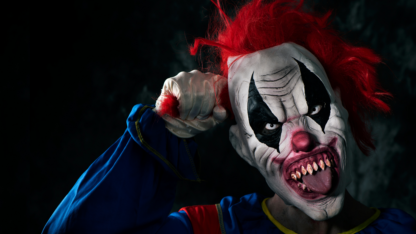 horror clown mask on black background pulling his red hair 