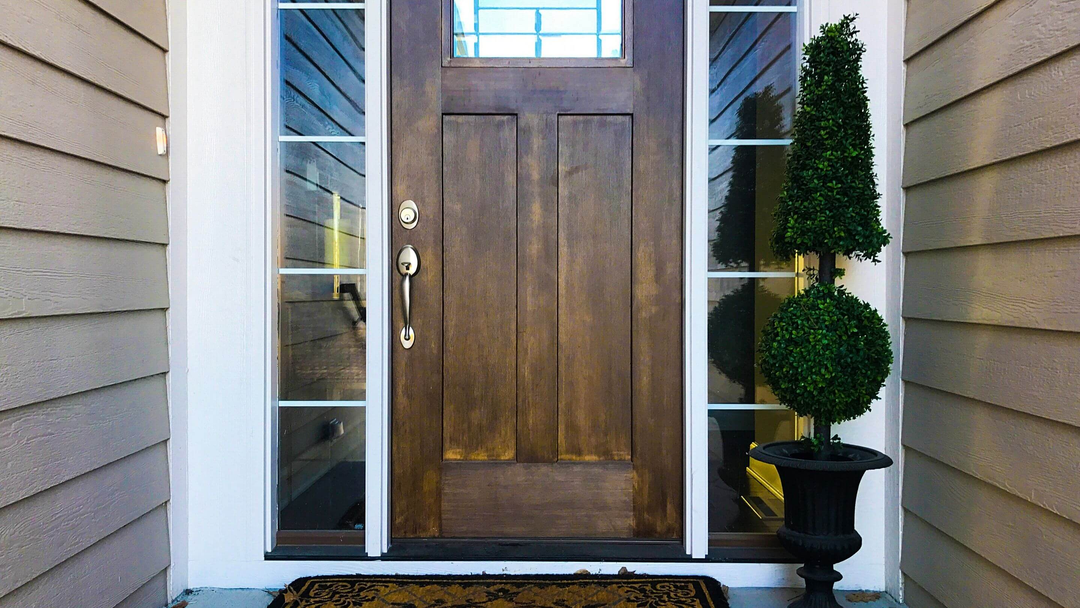 potted topiary tree on front porch in front of wooden door and glass panels