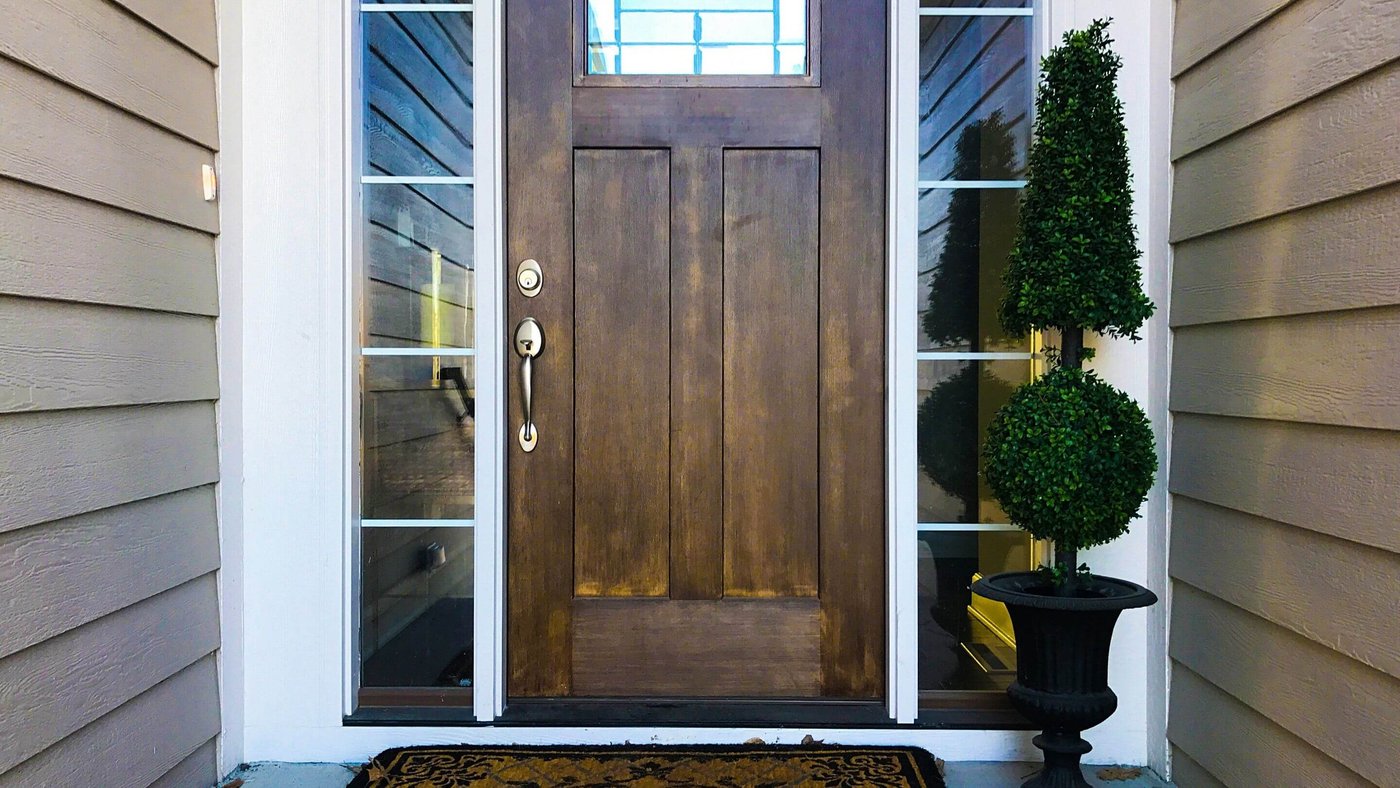 potted topiary tree on front porch in front of wooden door and glass panels