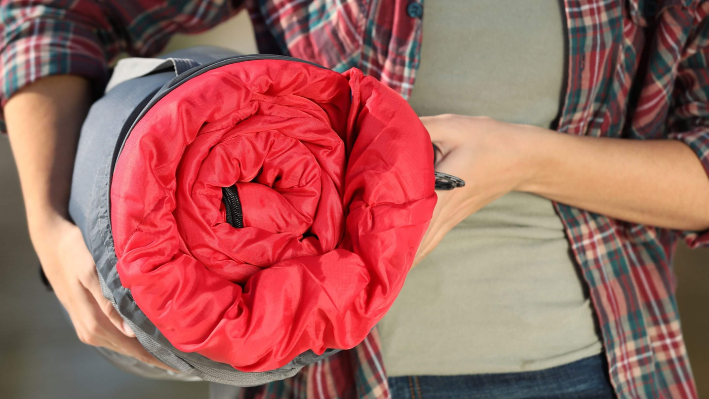 person carrying red sleeping bag rolled up