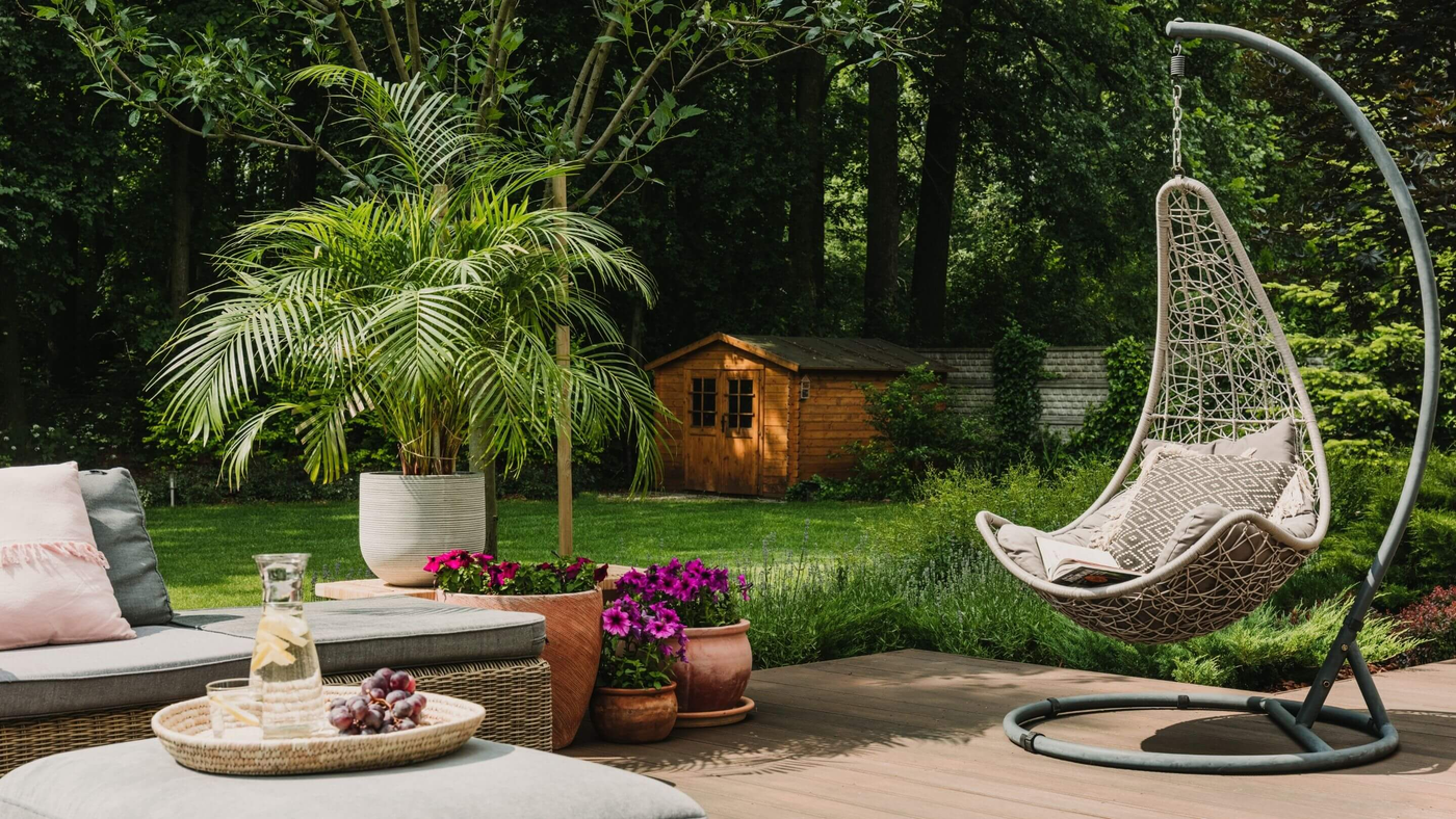 basket egg chair in garden space with shed and large fern plant in the background
