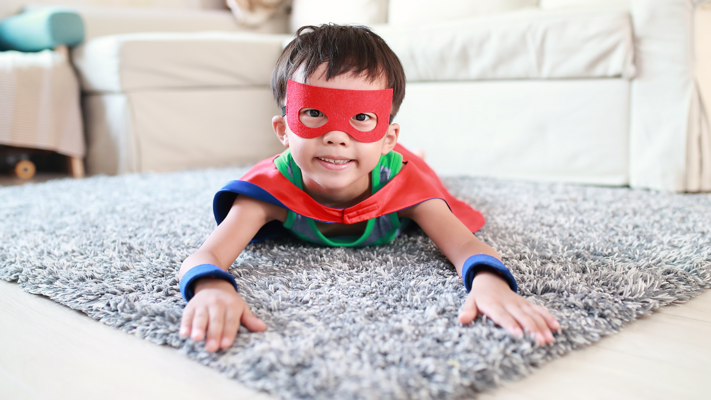 little boy dressed as super hero pretending to fly on living room rug