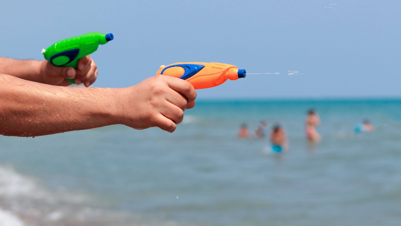 person at beach playing with two different coloured water guns
