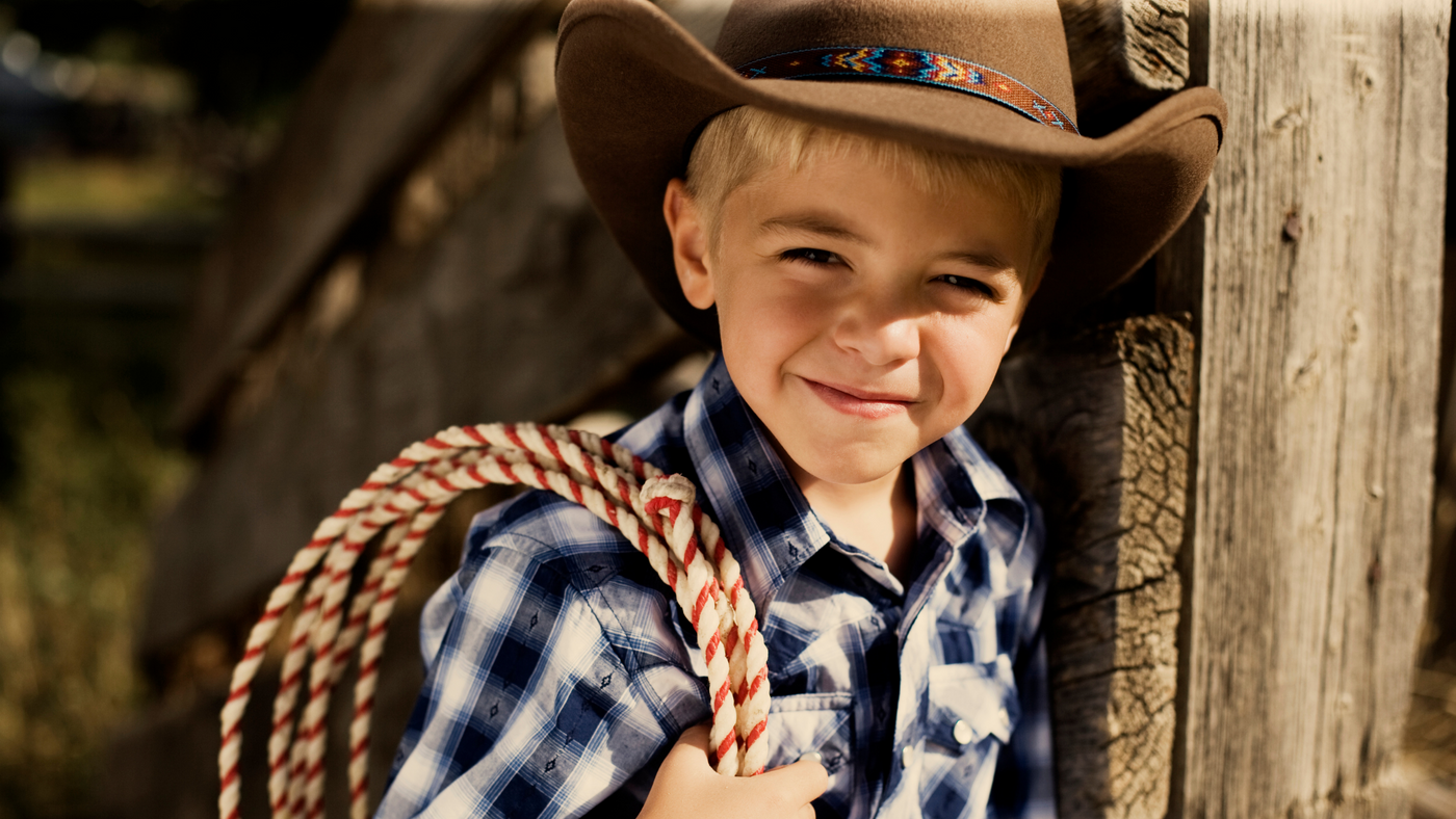 little boy dressed as a cowboy with cowboy hat, checked shirt and some rope