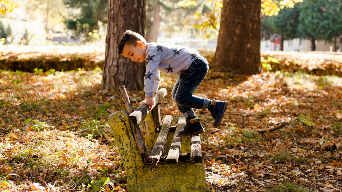 little boy playing on a park bench wearing a grey star print jumper