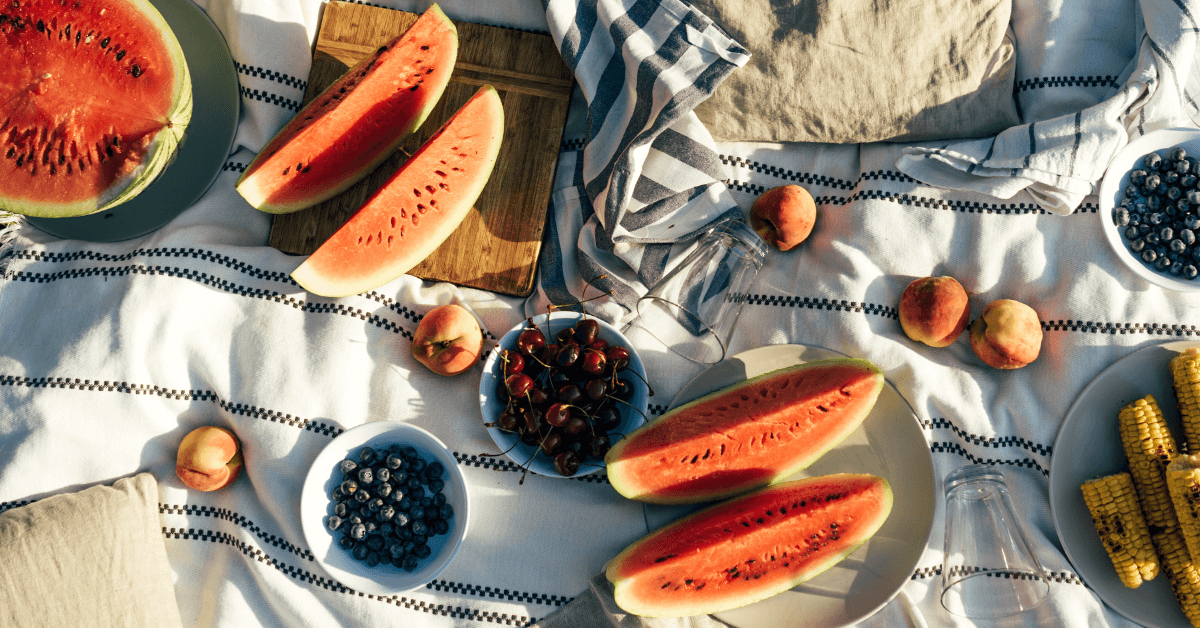 a variety of fruits in bowls on white and grey striped picnic blanket in the sunshine