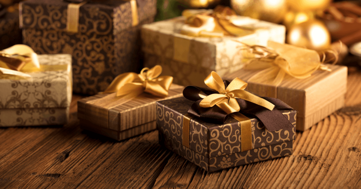 gold and black gift boxes placed under christmas tree, warm white lights in background - night time