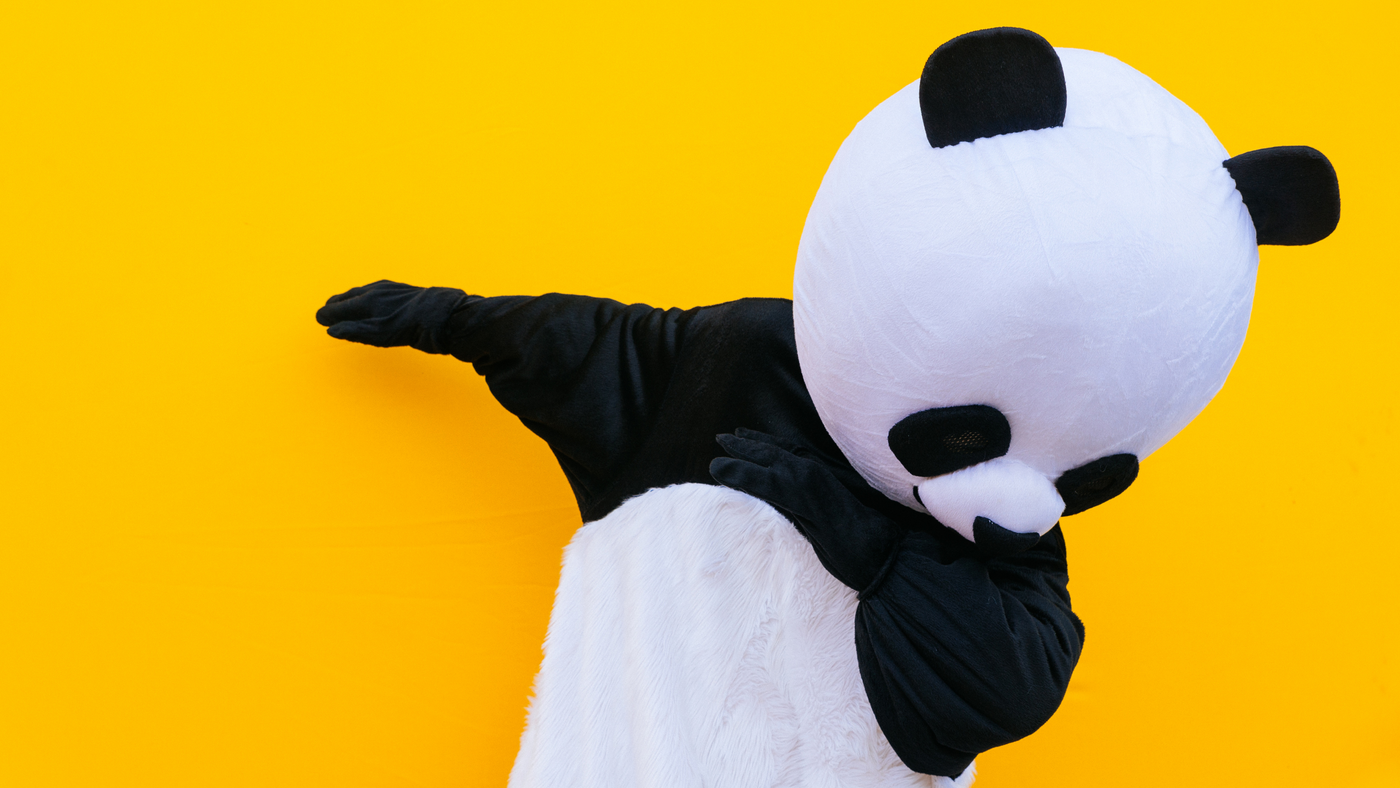 person wearing panda costume doing a dance move on yellow background