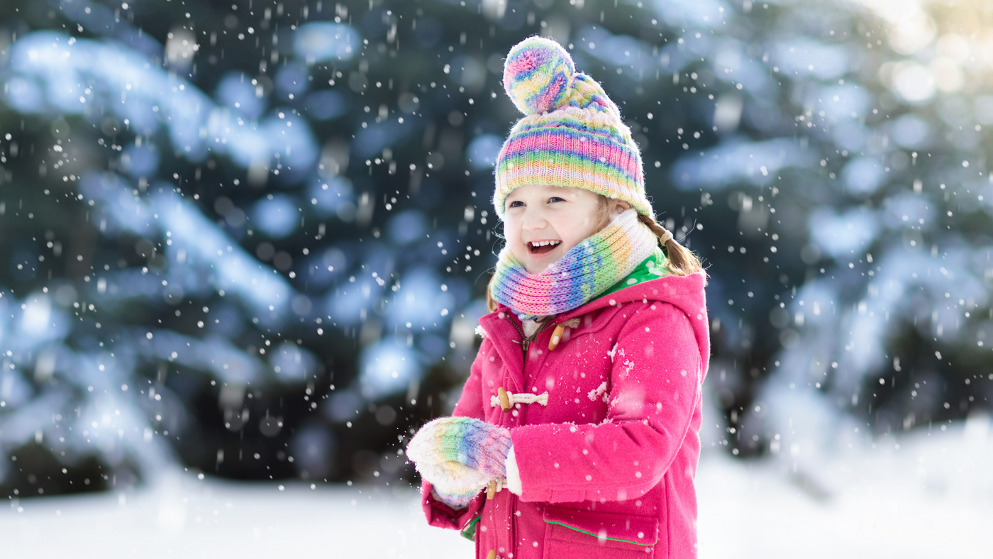 little girl playing in snow wearing pink jacket and multi colour hat scarf and glove set