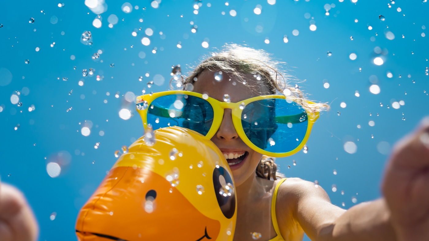 little girl wearing giant sunglasses on duck shaped inflatable with blue summer sky