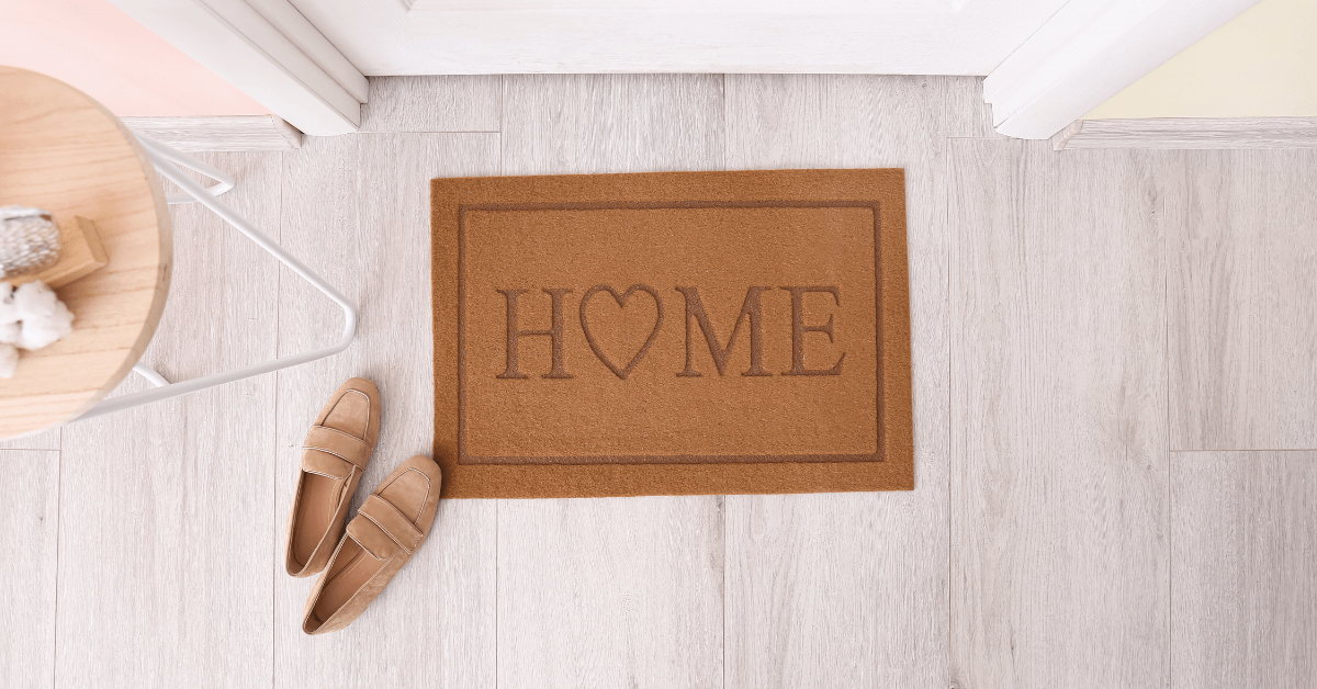 home slogan door mat with three sets of shoes on edge