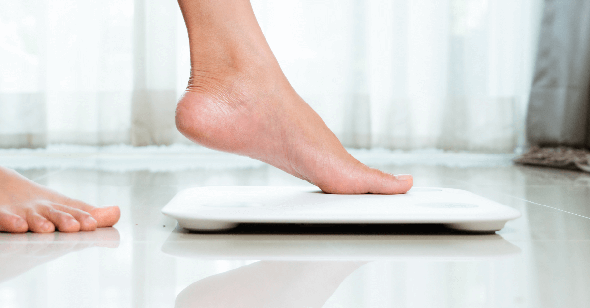 ladies foot stepping onto white electronic bathroom body scales in white bathroom space