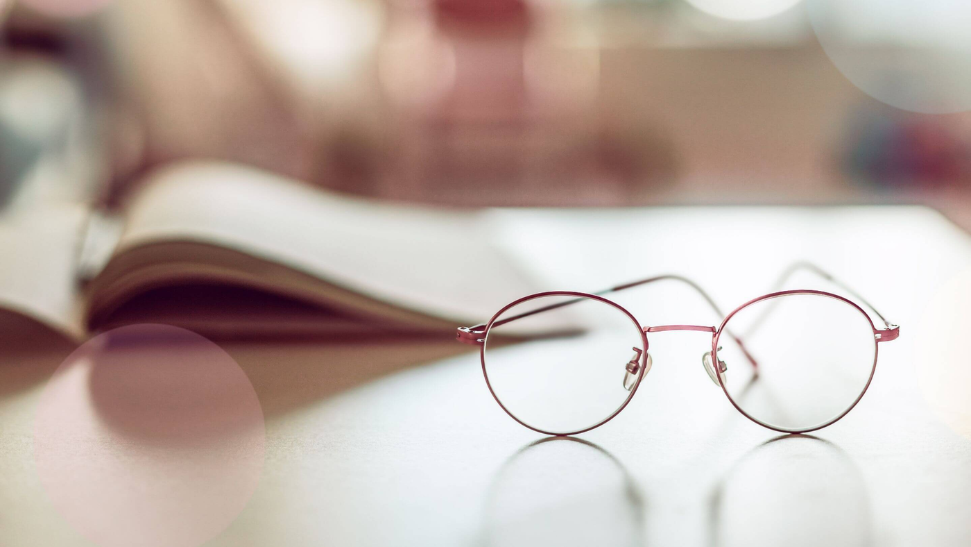 pair of pink rimmed glasses on a desk with open book in the background