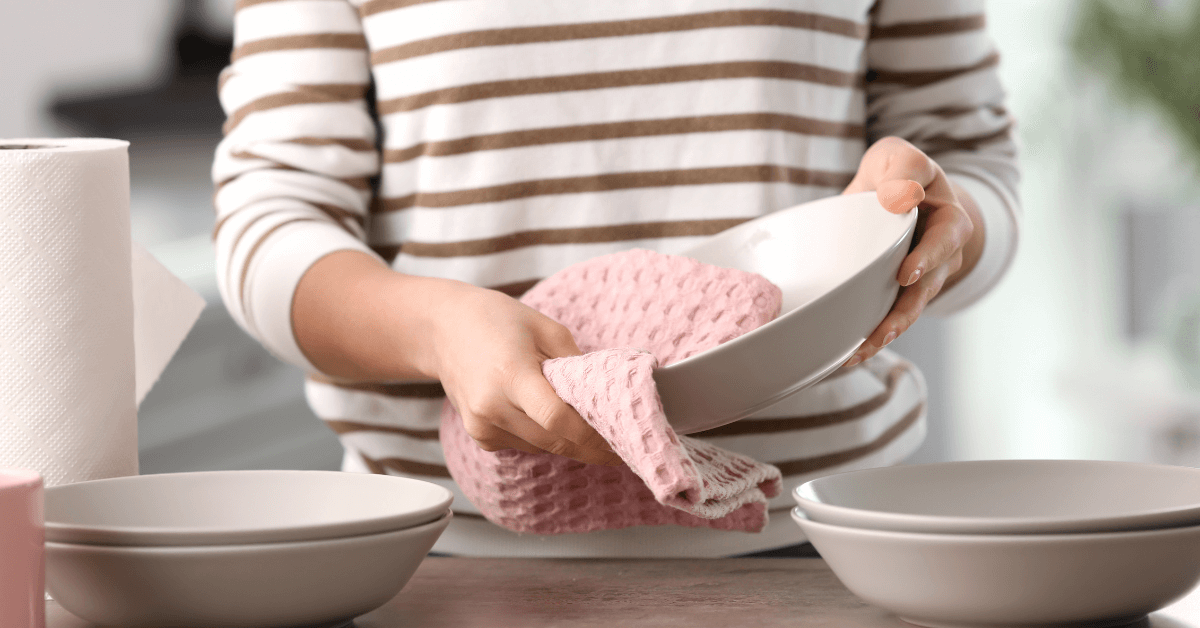 unidentified person using pink dish cloth to dry white bowl in kitchen