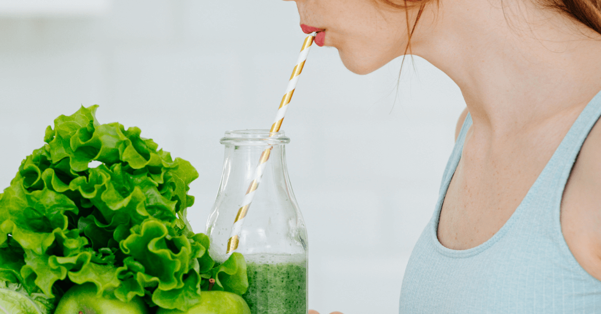 lady drinking green healthy smoothie from milk bottle through striped gold paper straw