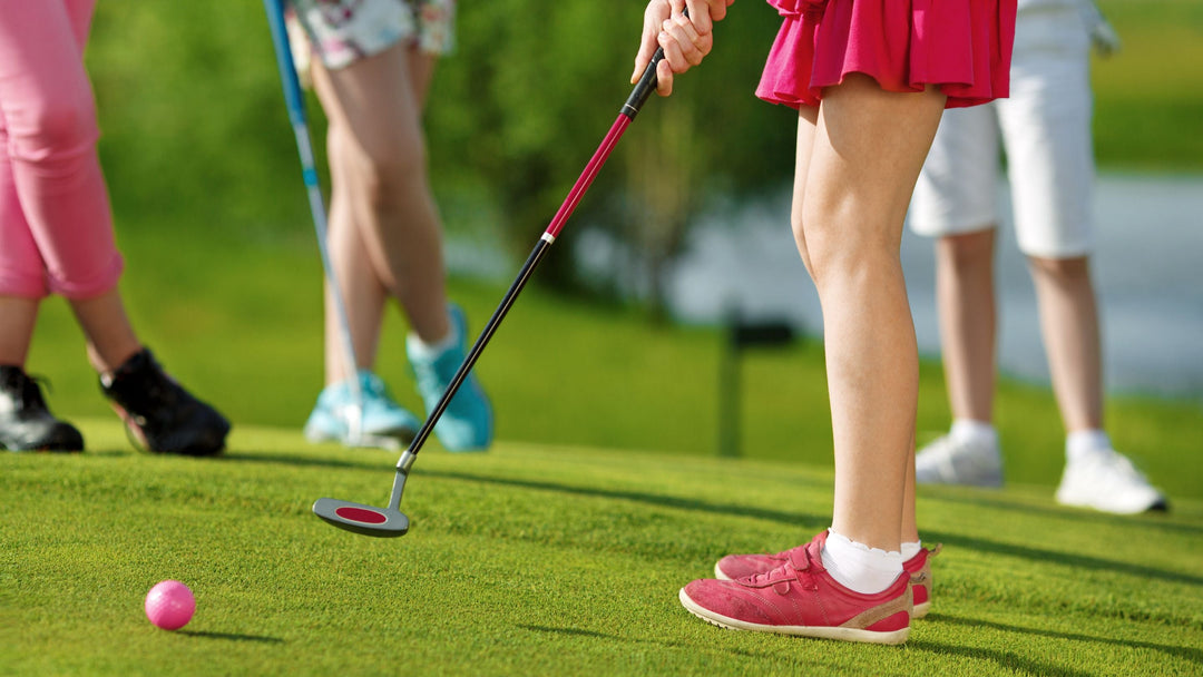 young girl uses pink gold glub to hit pink golf club on golf course with friends looking on