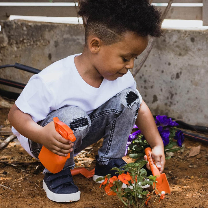 Boy in a garden using a kids trowel and plant spray