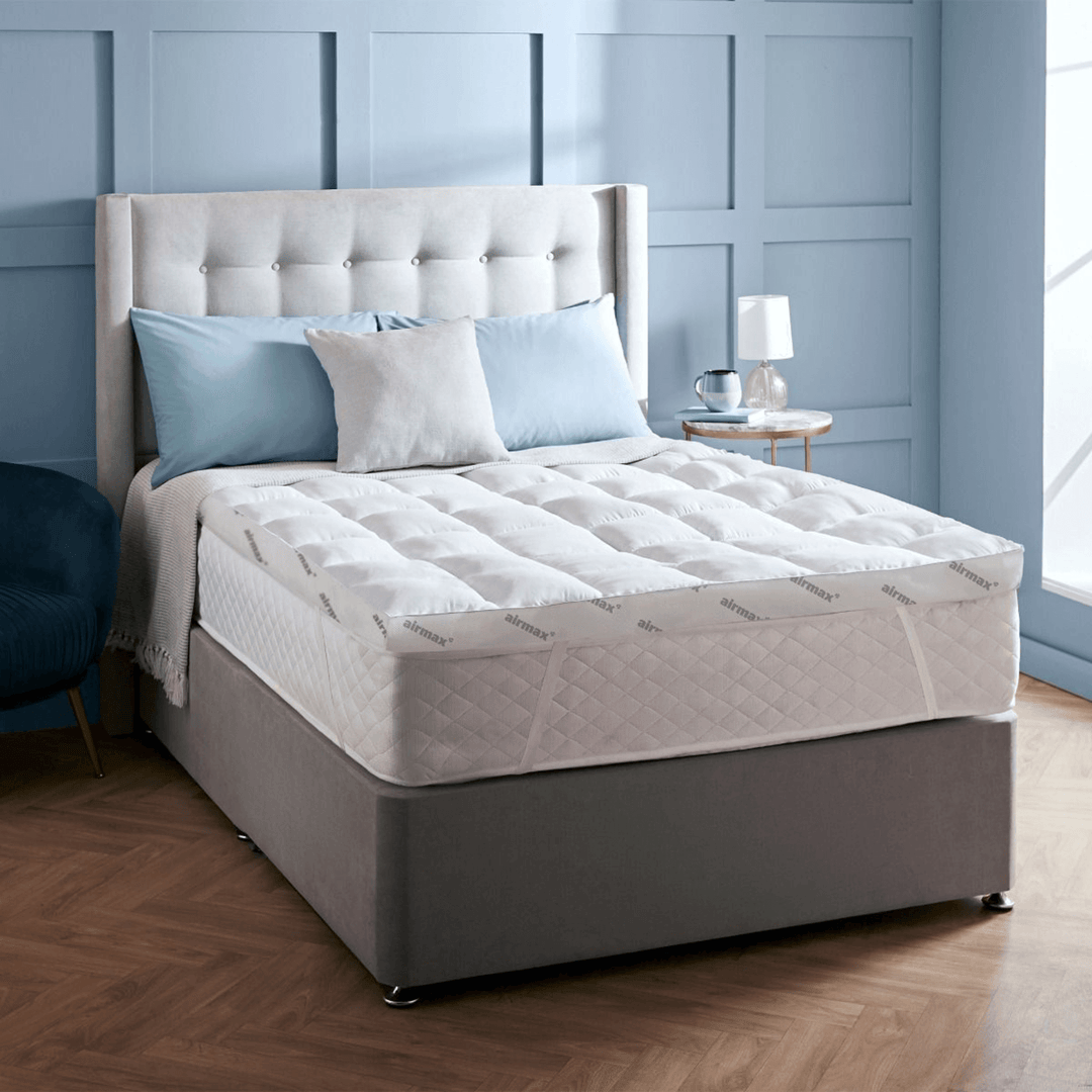 Mattress on a bed with pillows and a lamp in a room with blue paneled walls.