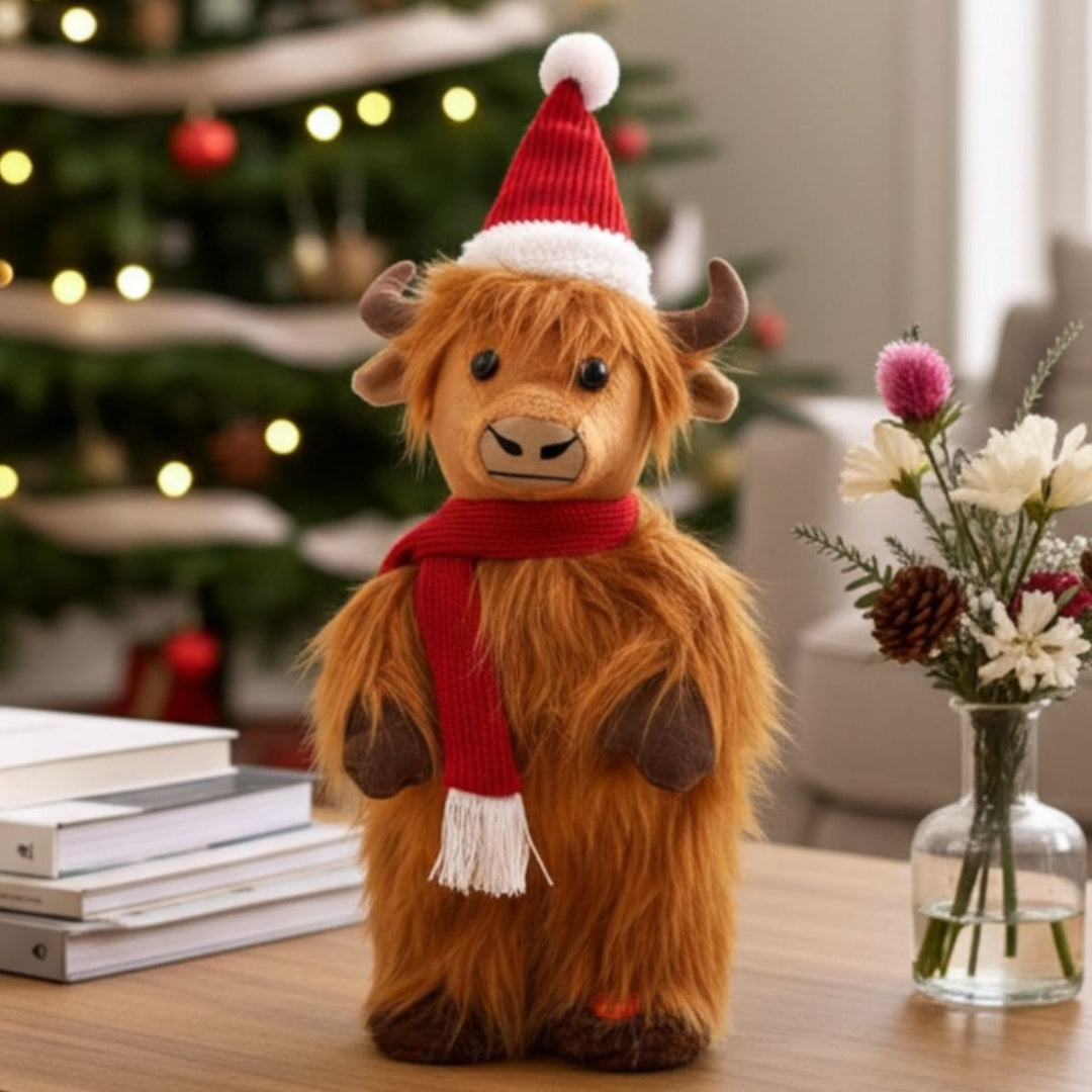 Plush Highland cow wearing a Santa hat and scarf in front of a decorated Christmas tree.