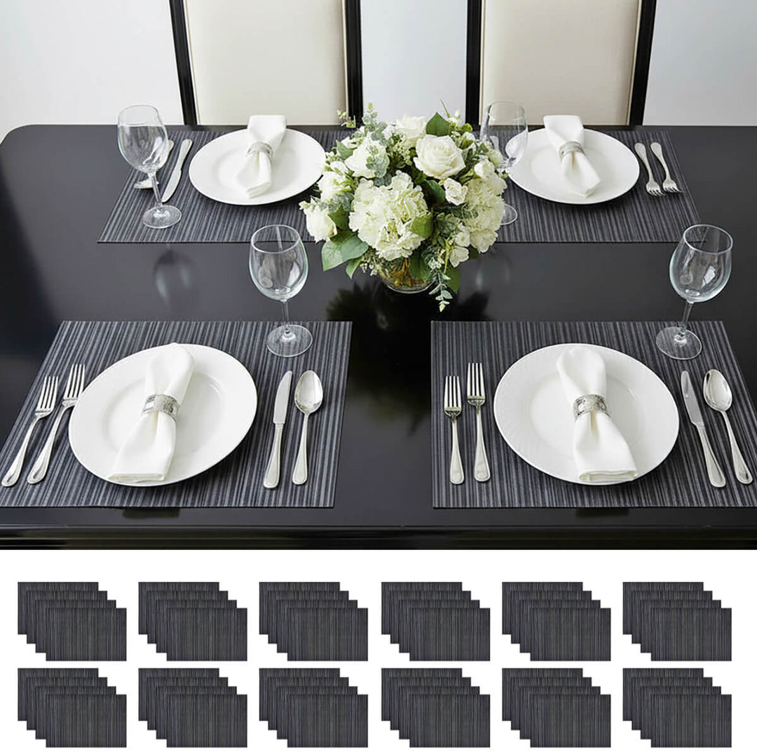Dining table set with black placemats, white plates, silverware, and a floral centerpiece.