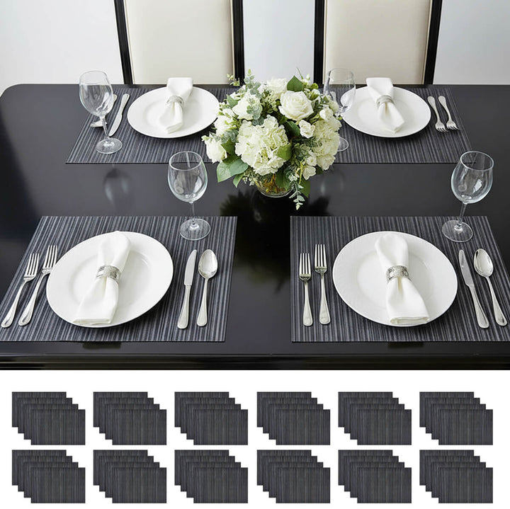 Dining table set with black placemats, white plates, silverware, and a floral centerpiece.