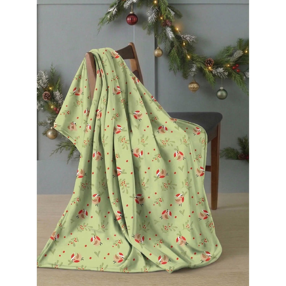 Christmas fleece blanket in green with robins and mistletoe pattern, draped over a chair with Christmas garland