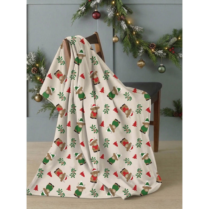 Christmas fleece blanket with Highland cow pattern, draped over a chair with Christmas garland