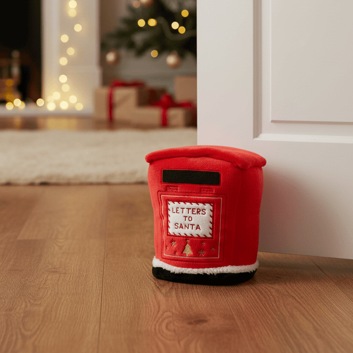 A red plush postman-shaped door stopper with a front patch reading &