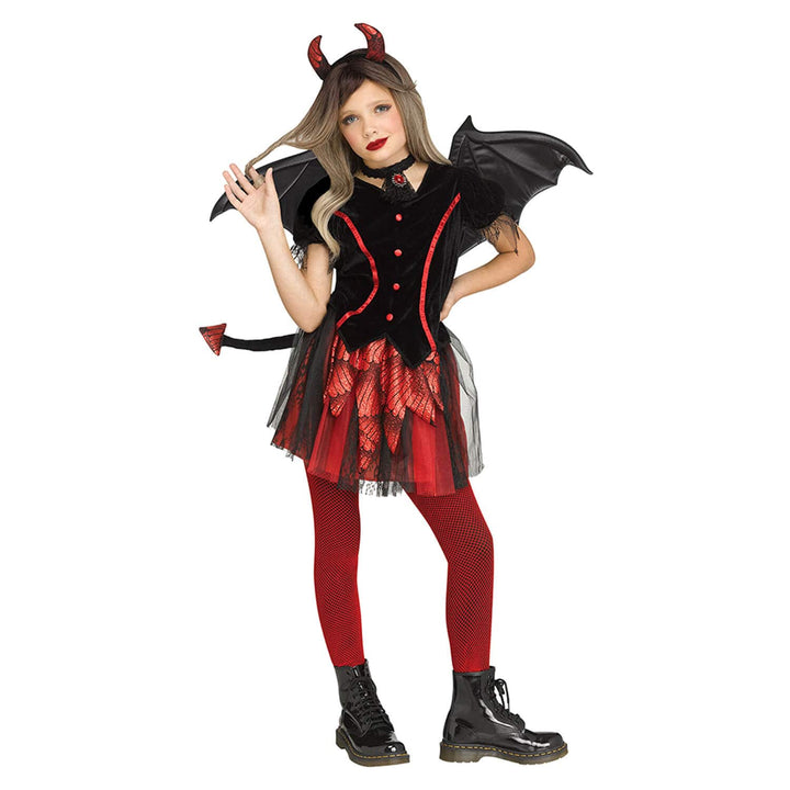 A child modelling a devil costume that includes a black top with red trim, a red patterned skirt overlay, red tights, black boots, black wings, a tail, and red horns.