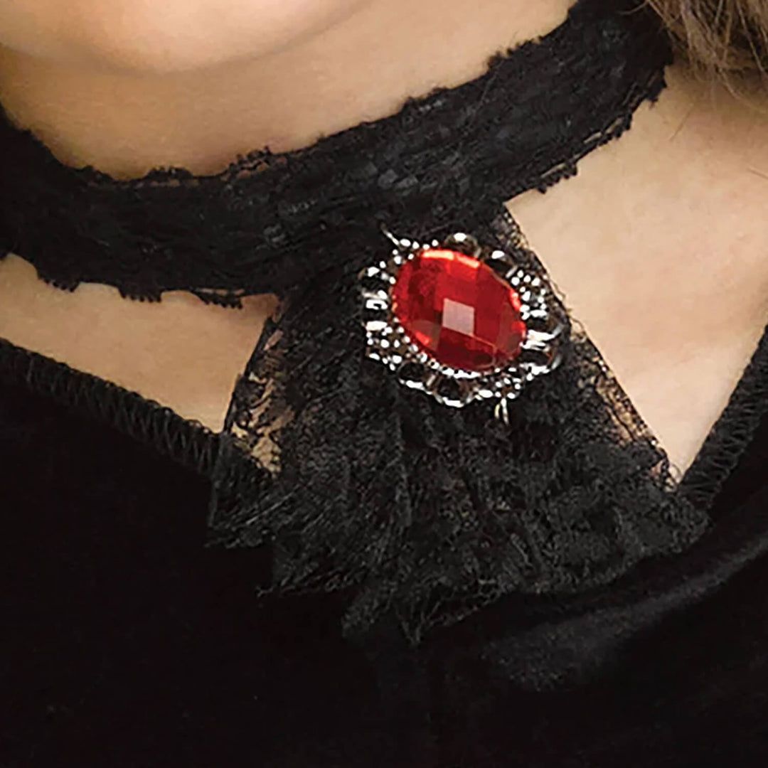 A close-up of a person wearing a black lace choker necklace with a large red oval gemstone brooch at the center.