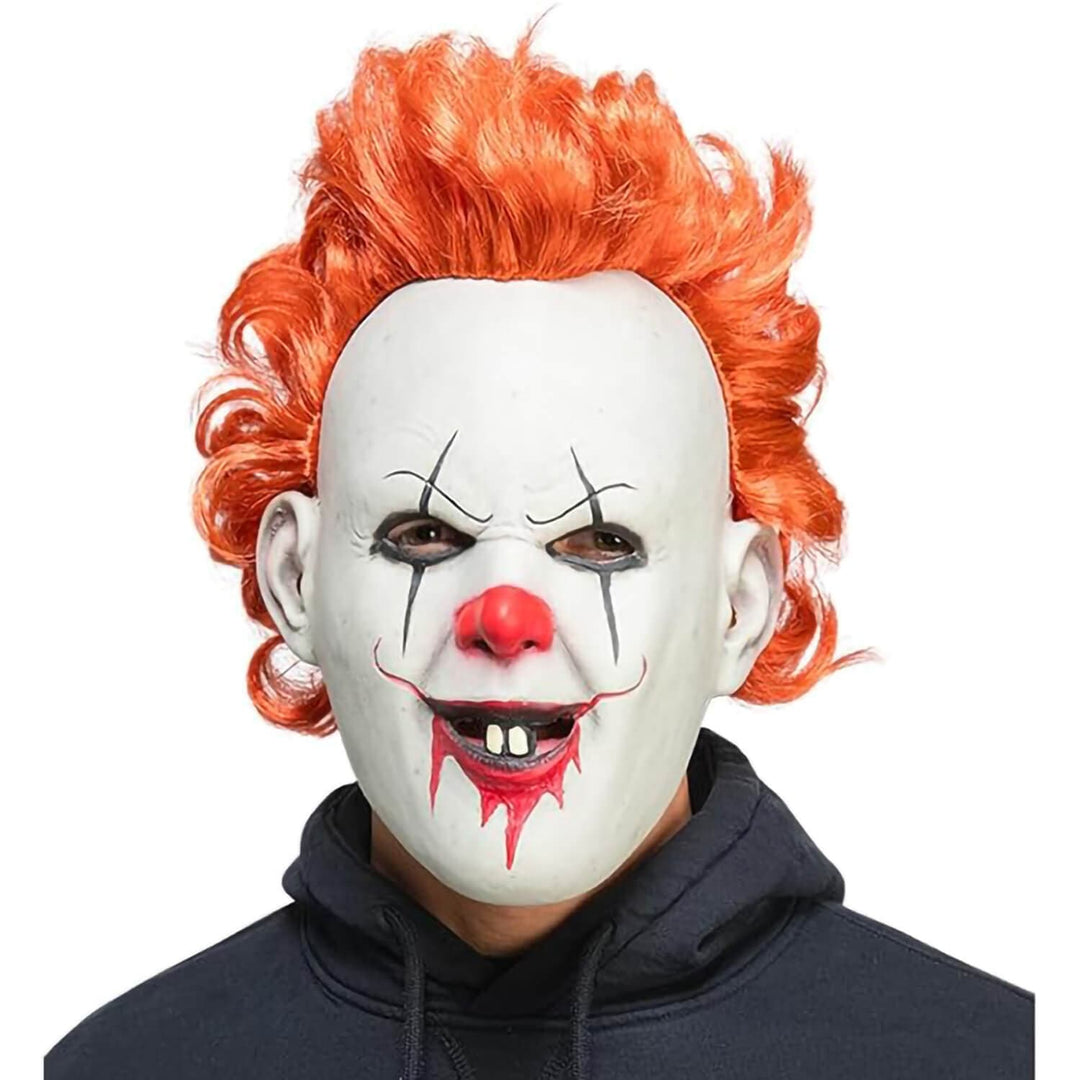 A person wearing a horror clown mask with white face paint, a red nose and lips, and bright orange curly hair, paired with a dark hoodie against a plain white background.