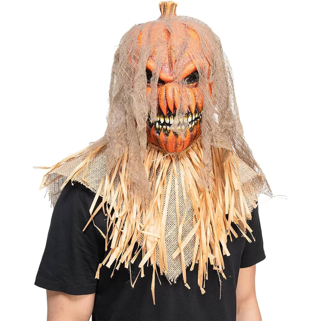 A scary Halloween scarecrow mask with a carved orange pumpkin head, tattered beige netting, and straw-colored hair, shown worn by a person against a plain white background.