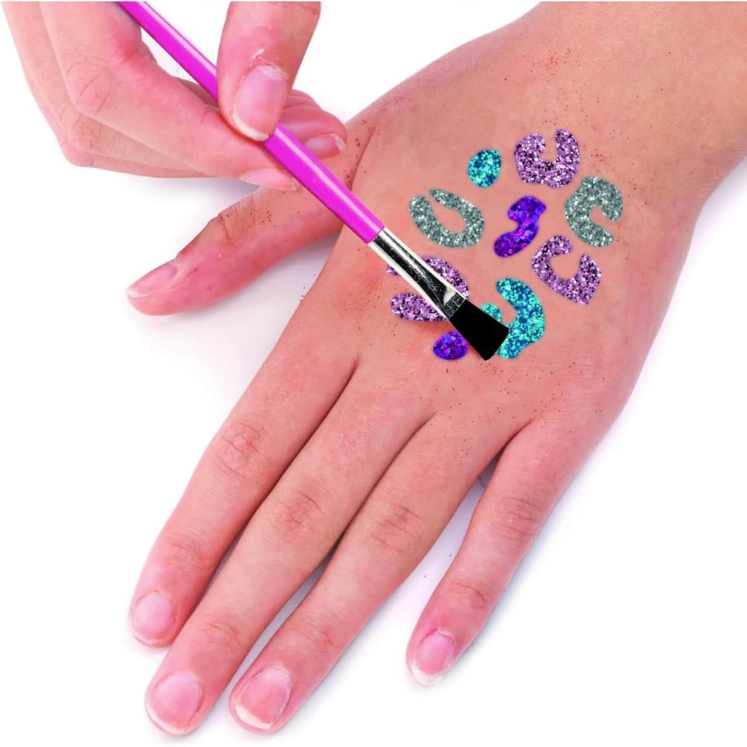 Person using a paint brush to create glitter tattoos on her hand