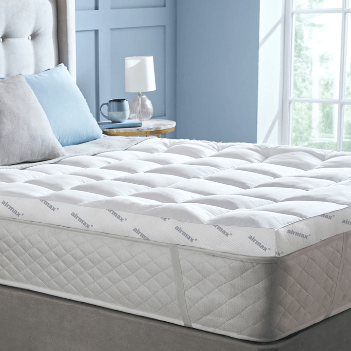 Mattress topper on a bed in a bedroom setting with a lamp and pillows.