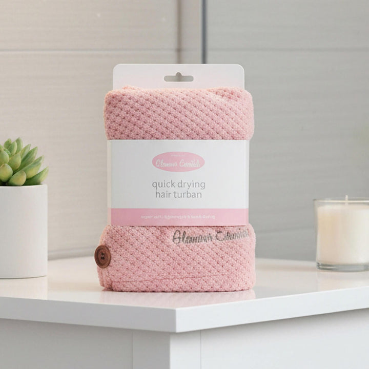 Pink quick drying hair turban in packaging on a shower room cabinet with candle and plant
