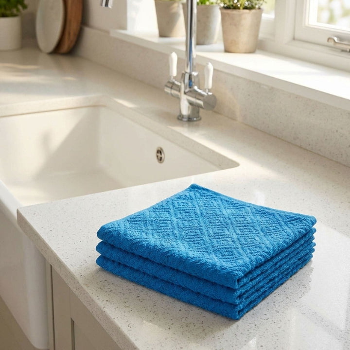 Stack of blue towels on a kitchen counter with a sink and window in the background