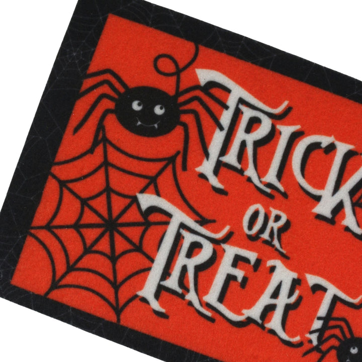 A close-up of a Halloween-themed decorative mat with a bright red background, black spider and spiderweb graphics, and large white gothic text reading 'TRICK OR TREAT'.