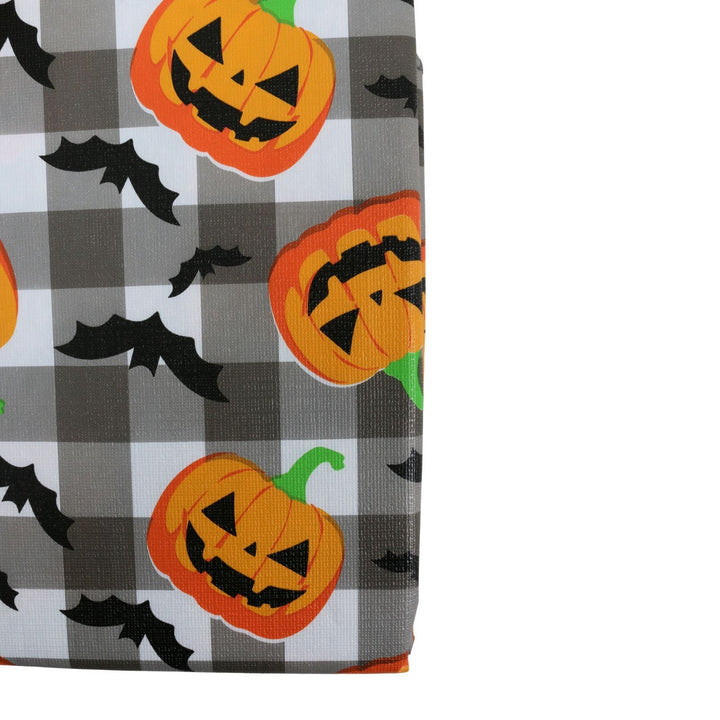 A close-up of tablecover swatch featuring a Halloween buffalo plaid pattern in gray, white, and black, decorated with orange jack-o'-lantern pumpkins and black bats.