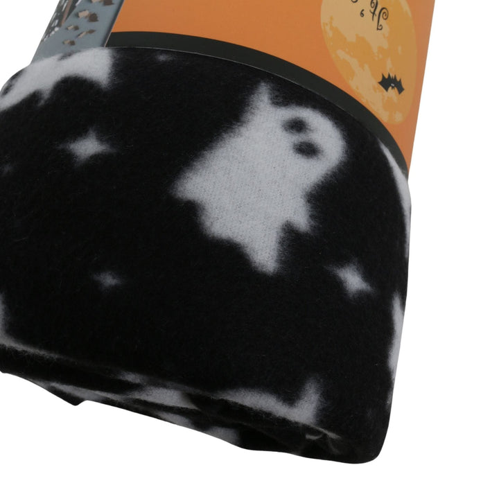 A close-up of a rolled blanket featuring a black and white ghost and star pattern, wrapped in an orange paper band with Halloween-themed graphics.