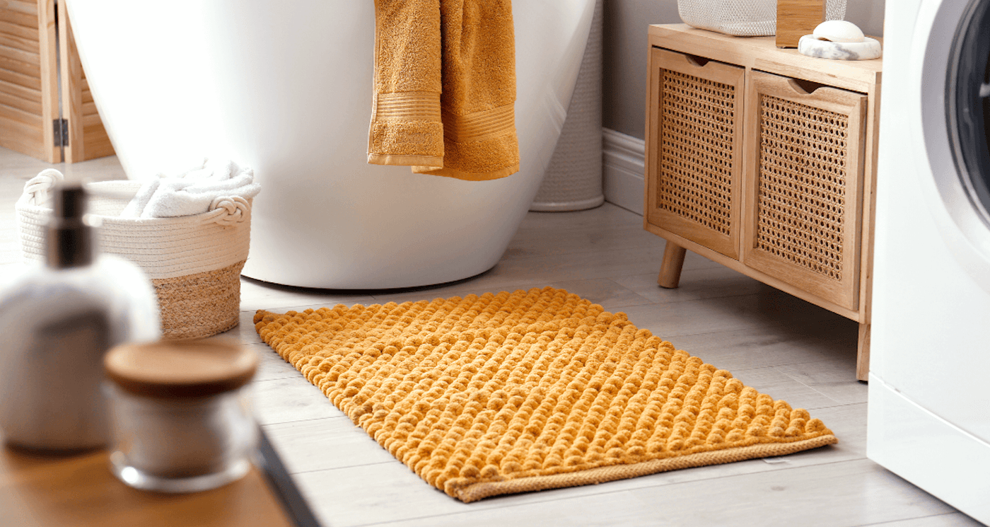 yellow bath mat on bathroom floor beside bath tub with matching yellow towel draping over the edge