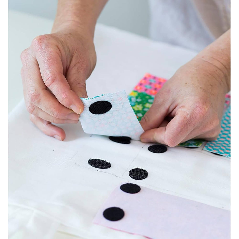 Hands applying self adhesive black velcro pads to sections of fabric