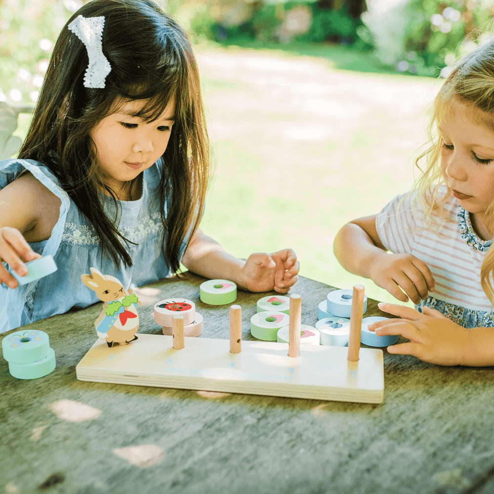 two little girls play with peter rabbit counting game in garden on wooden picnic bench