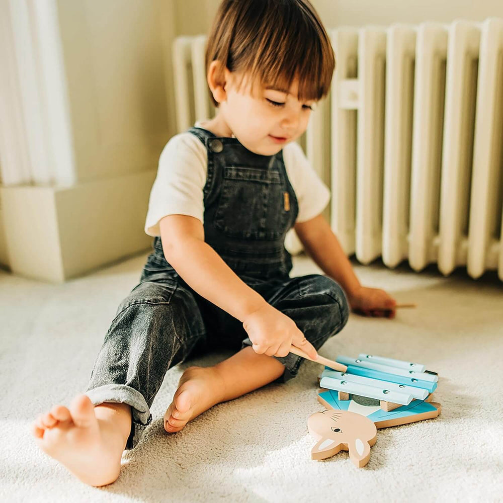 Toddler playing on the floor with a Peter Rabbit xylophone with 5 bars and 2 drumsticks