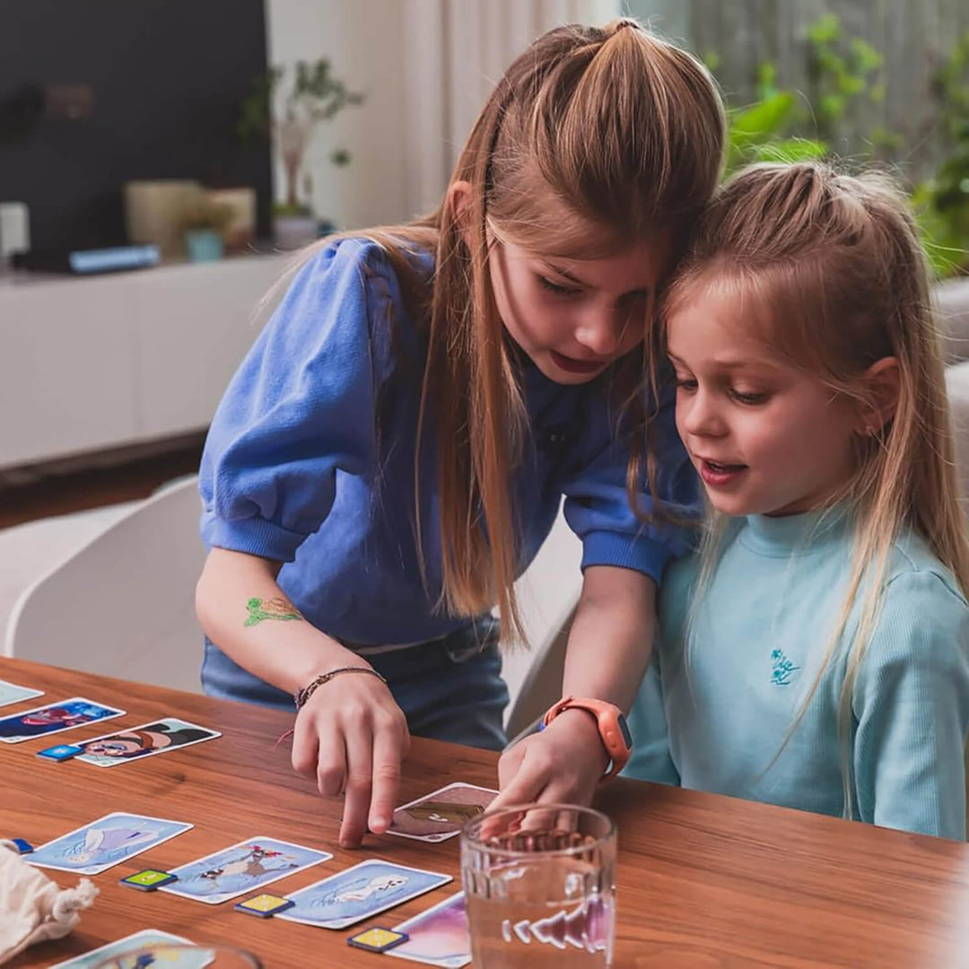 Two young girls playing a card game together at a table.