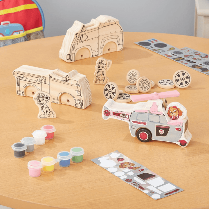 craft set contents laid out on wooden table top includes paint tubs, foil sticker sheets and wooden blocks and parts