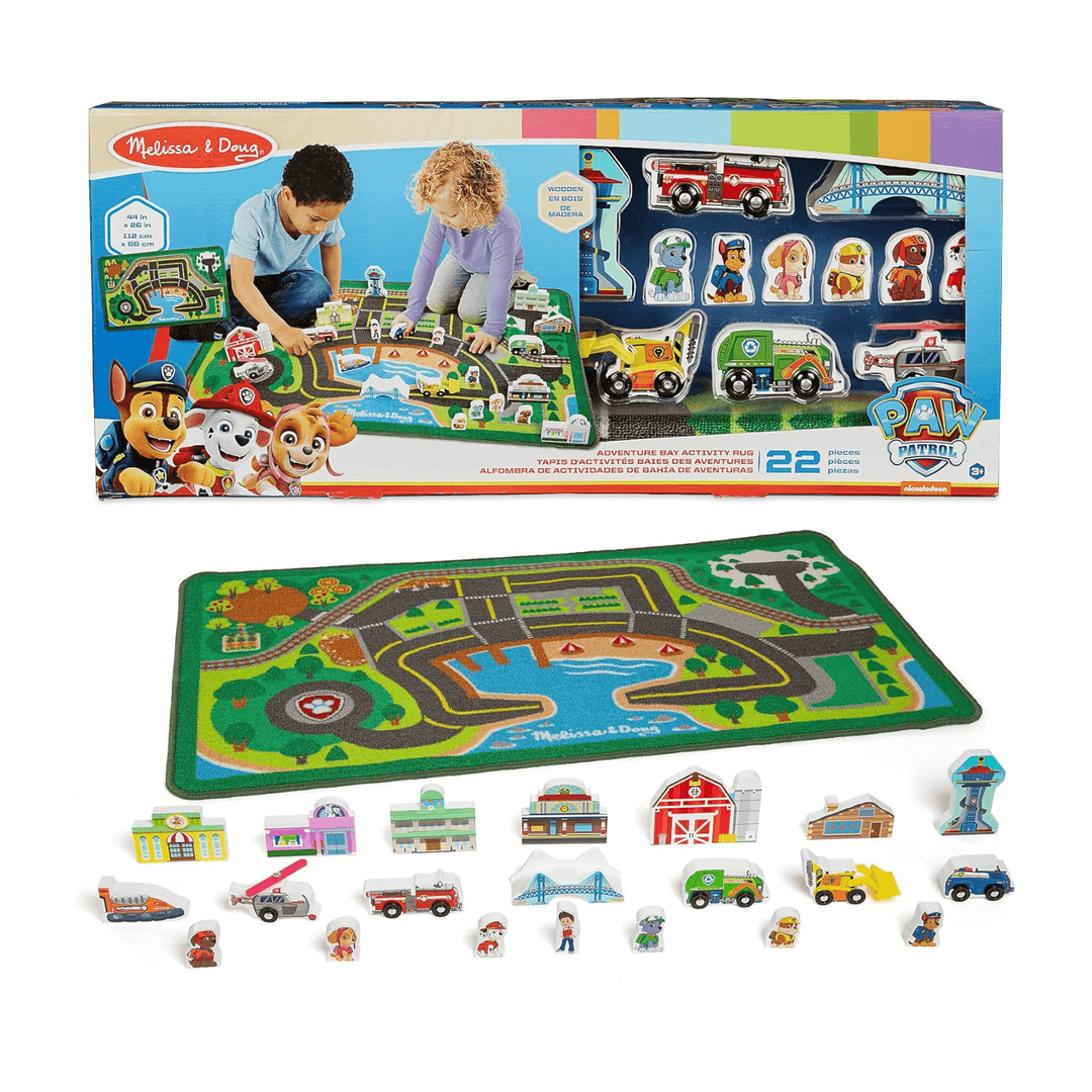 PAW Patrol adventure bay activity rug in cardboard packaging with includes wooden figures, buildings and vehicles laid out beside printed rug on white background